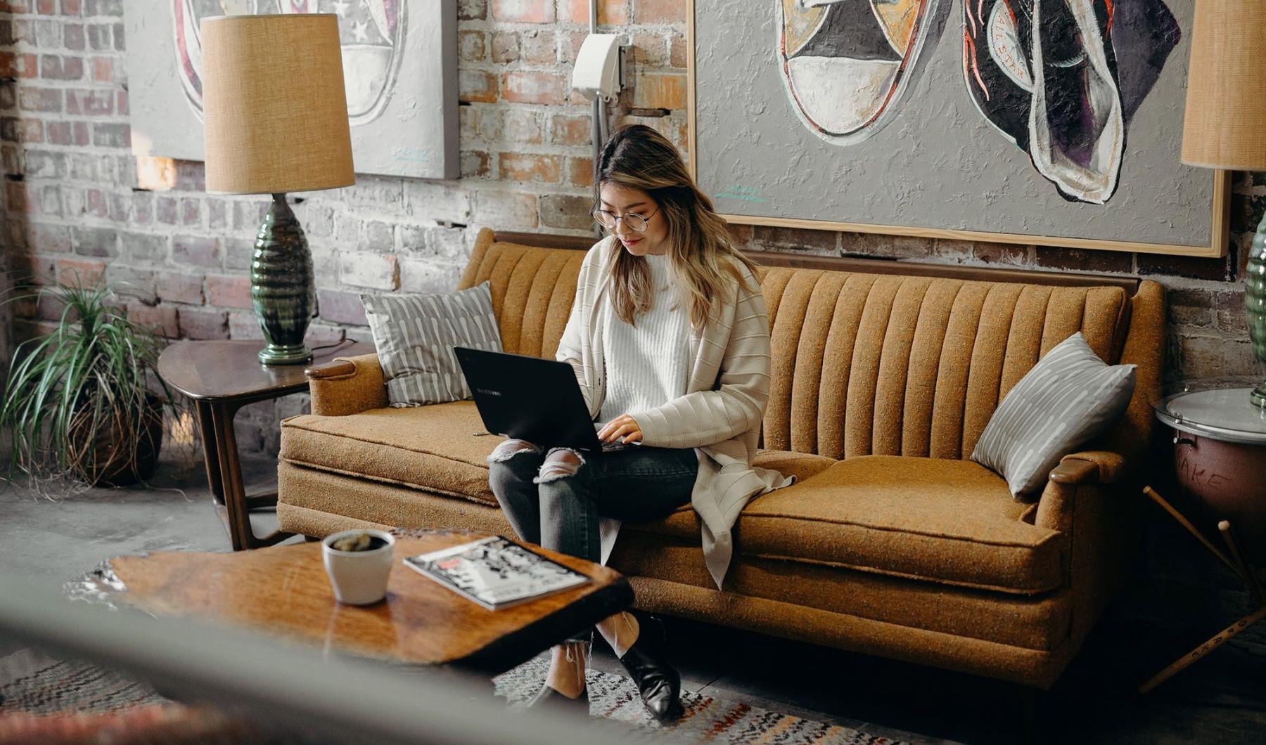 a woman sitting on a couch working on a laptop