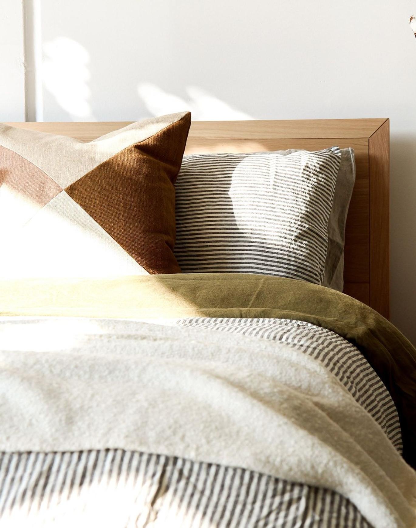 swath of sunlight shines across a well made bed and bedside table with a vase of cotton plants